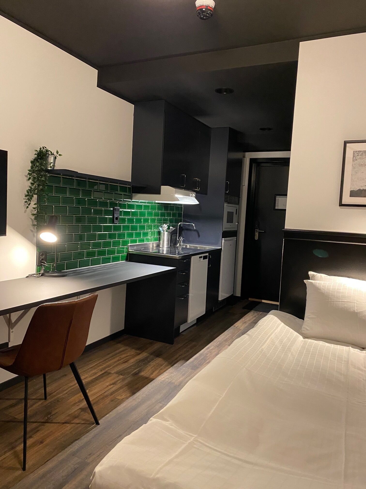 A modern kitchen with a green backsplash, a dining area with a chair, and a bed with white bedding.