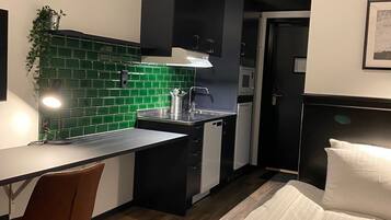 A modern kitchen with a green backsplash, a dining area with a chair, and a bed with white bedding.