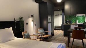 A hotel room with a bed, two chairs, a desk, a kitchenette, and a modern design.