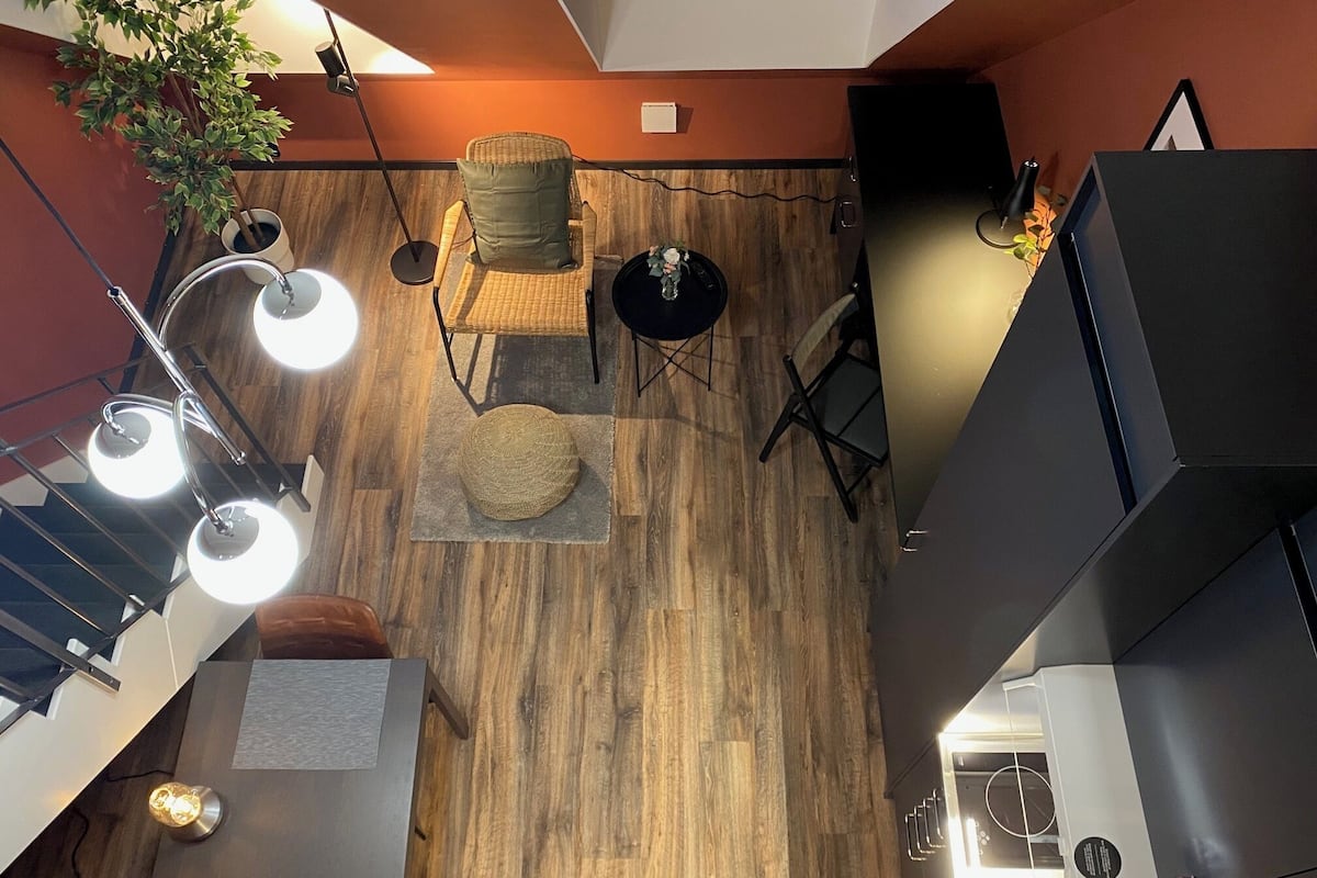 A modern interior with a wooden floor, a wicker chair with a cushion, a small round table, and a potted plant.