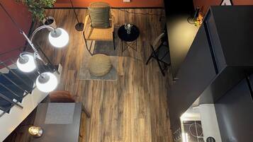 Un interior moderno con piso de madera, una silla de mimbre con cojín, una mesita redonda y una planta en maceta.