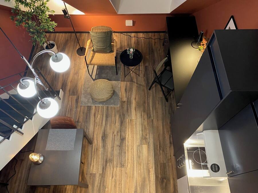Un interior moderno con piso de madera, una silla de mimbre con cojín, una mesita redonda y una planta en maceta.