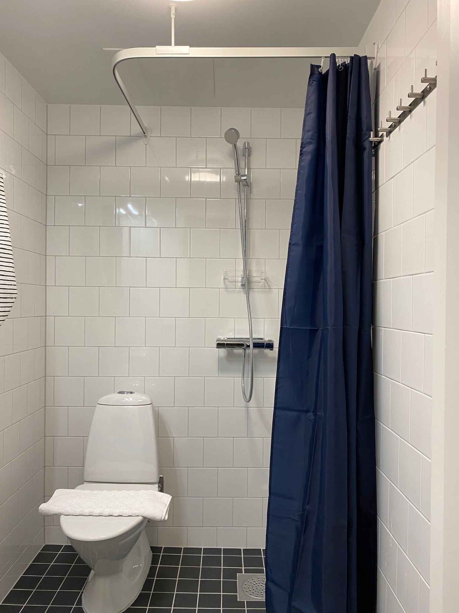 Une petite salle de bain moderne avec des carreaux blancs, une douche dotée d’un pommeau de douche incurvé, des toilettes et un rideau de douche bleu.