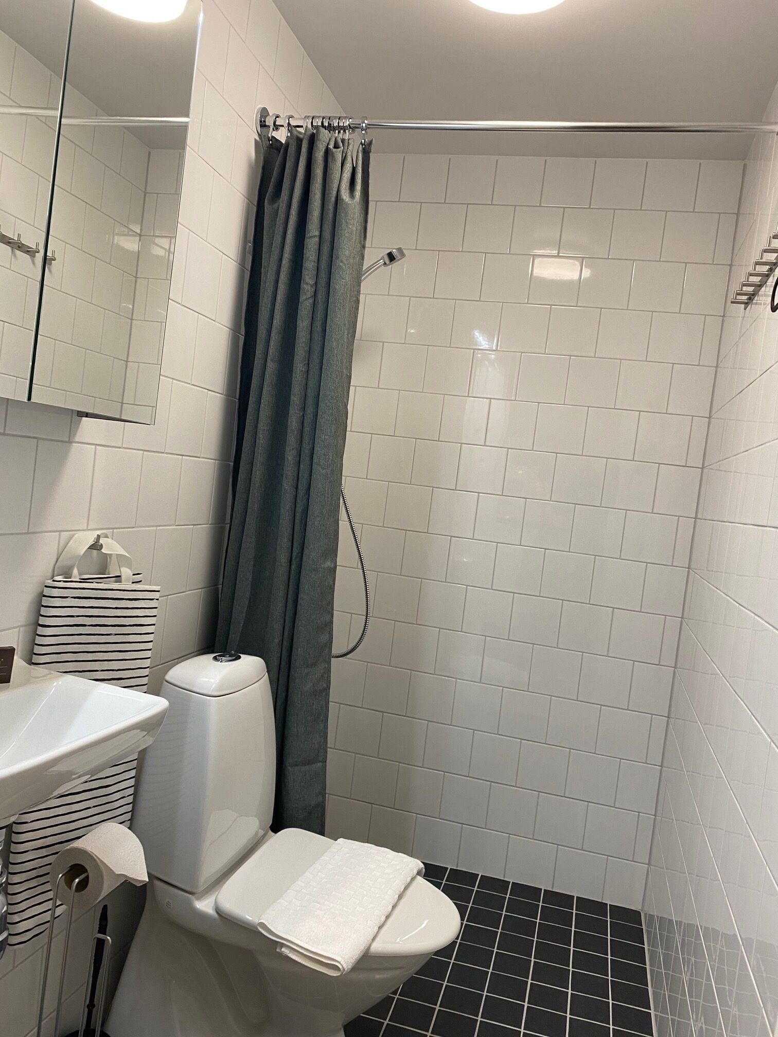 Une salle de bain avec des murs carrelés de carreaux blancs, un rideau de douche, des toilettes et un lavabo.