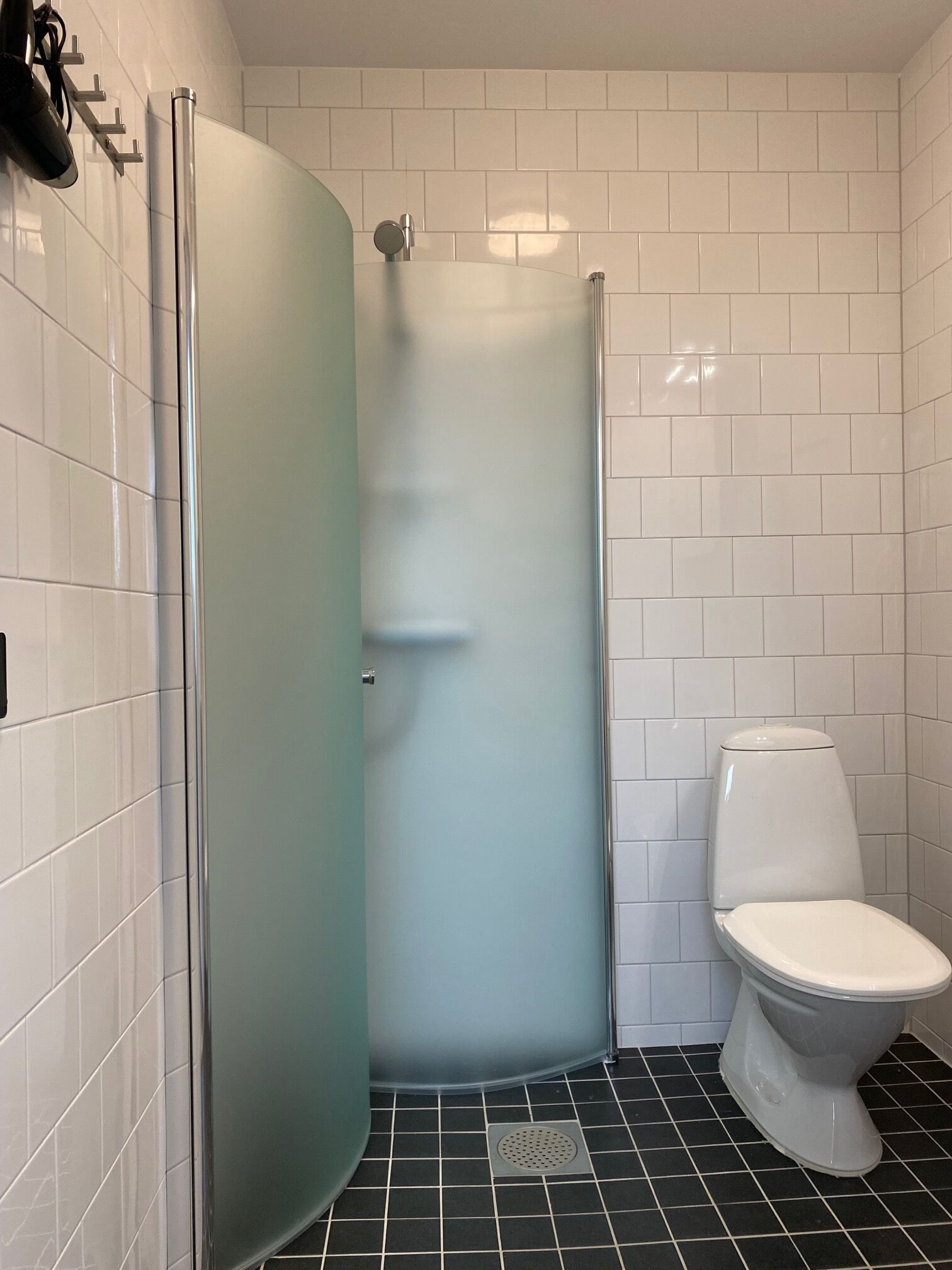 Une salle de bain avec des toilettes blanches, une douche en verre et un carrelage noir au sol.