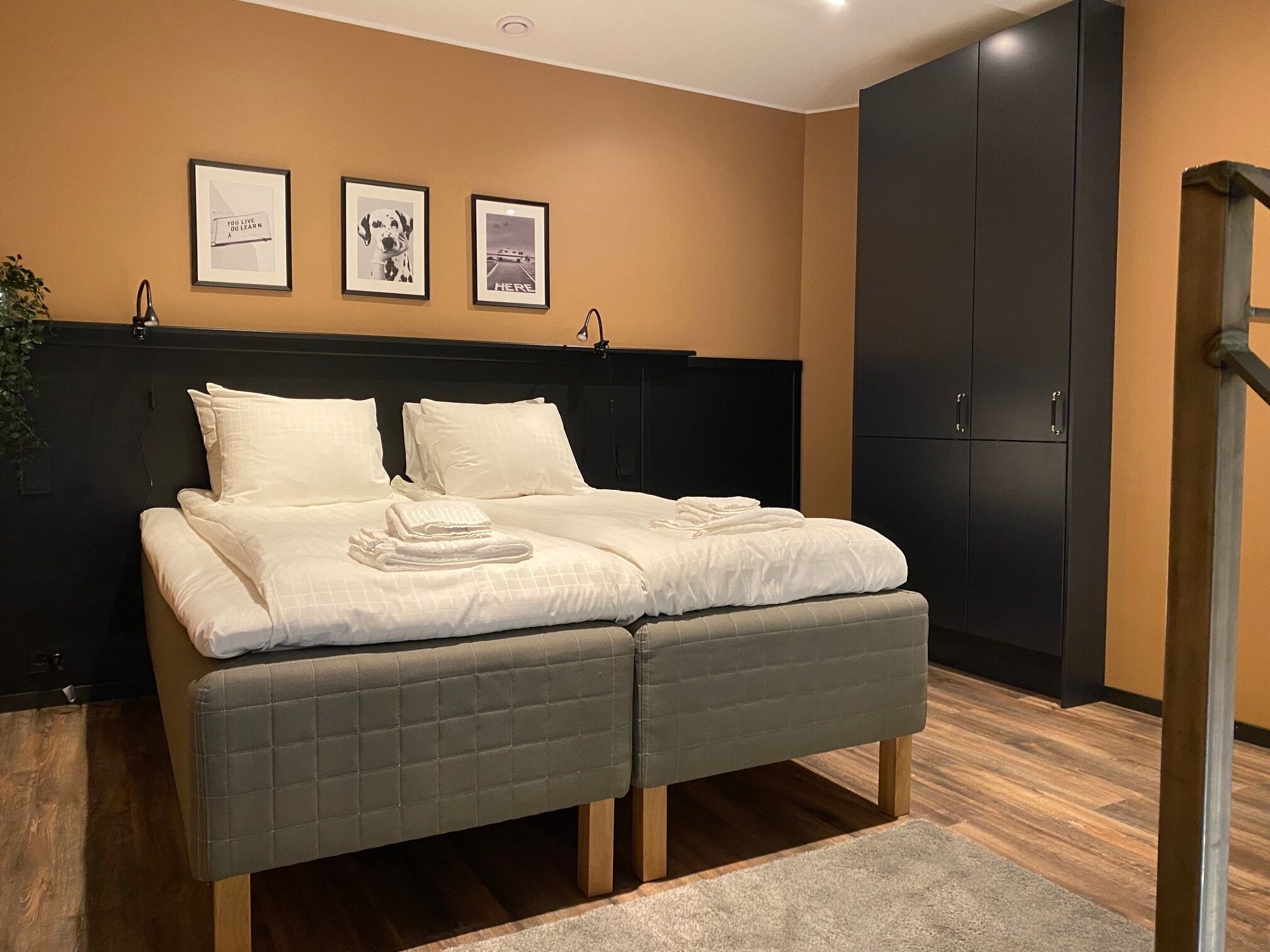 A modern bedroom with a bed, a dark wardrobe, and three framed pictures on the wall.