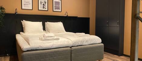 A modern bedroom with a bed, a dark wardrobe, and three framed pictures on the wall.