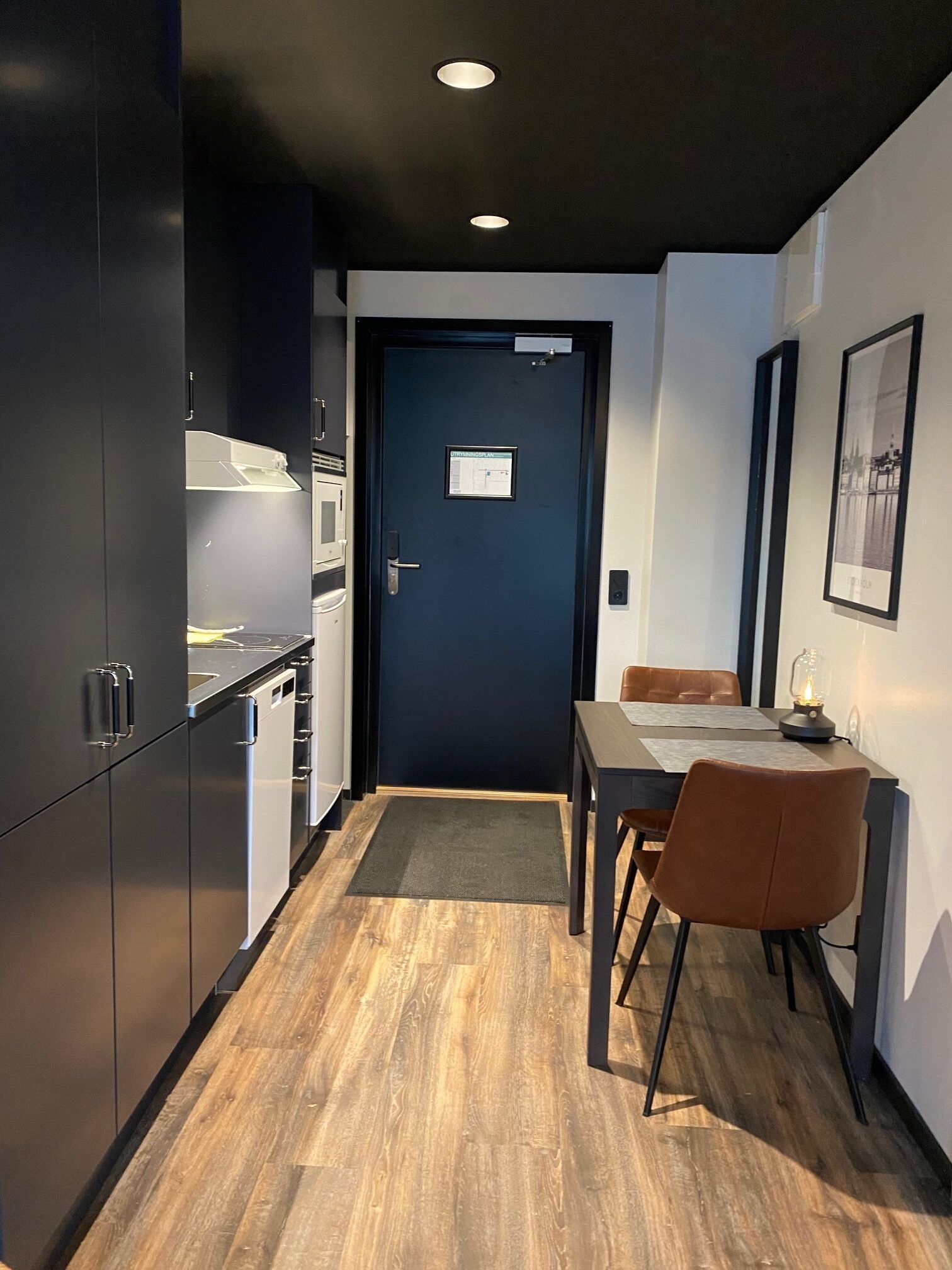 A modern kitchen with dark cabinets, a dining area with a table and chairs, and a door with a sign.