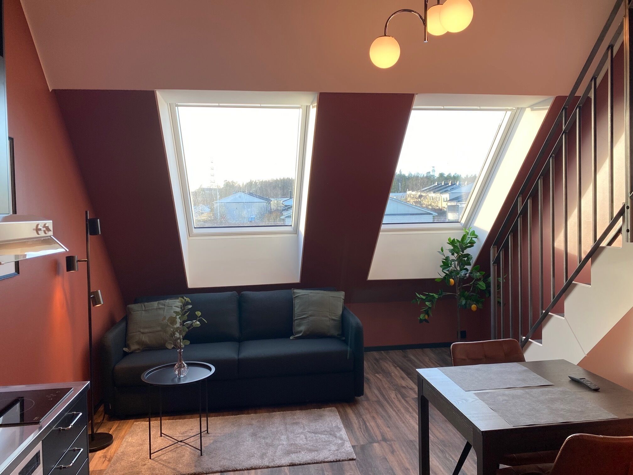 Un appartement moderne de style « loft », avec un canapé noir, une table à manger et un escalier.