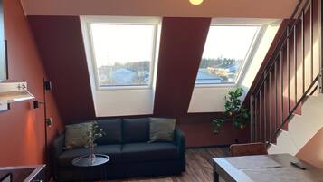 Un appartement moderne de style « loft », avec un canapé noir, une table à manger et un escalier.