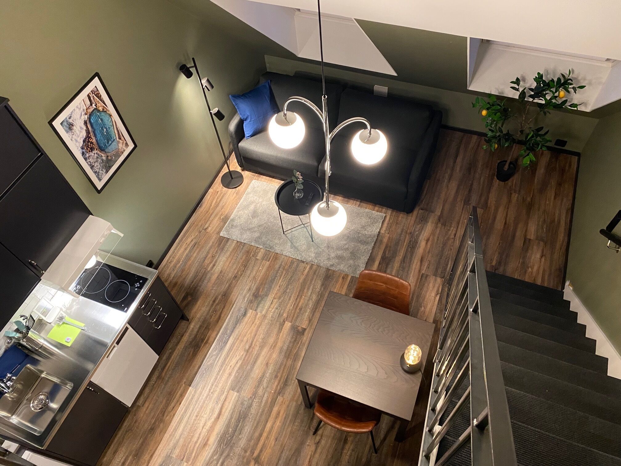 Een moderne keuken met een inbouwfornuis, een eethoek met tafel en stoelen, een trap en een zithoek met een bank en een hanglamp.