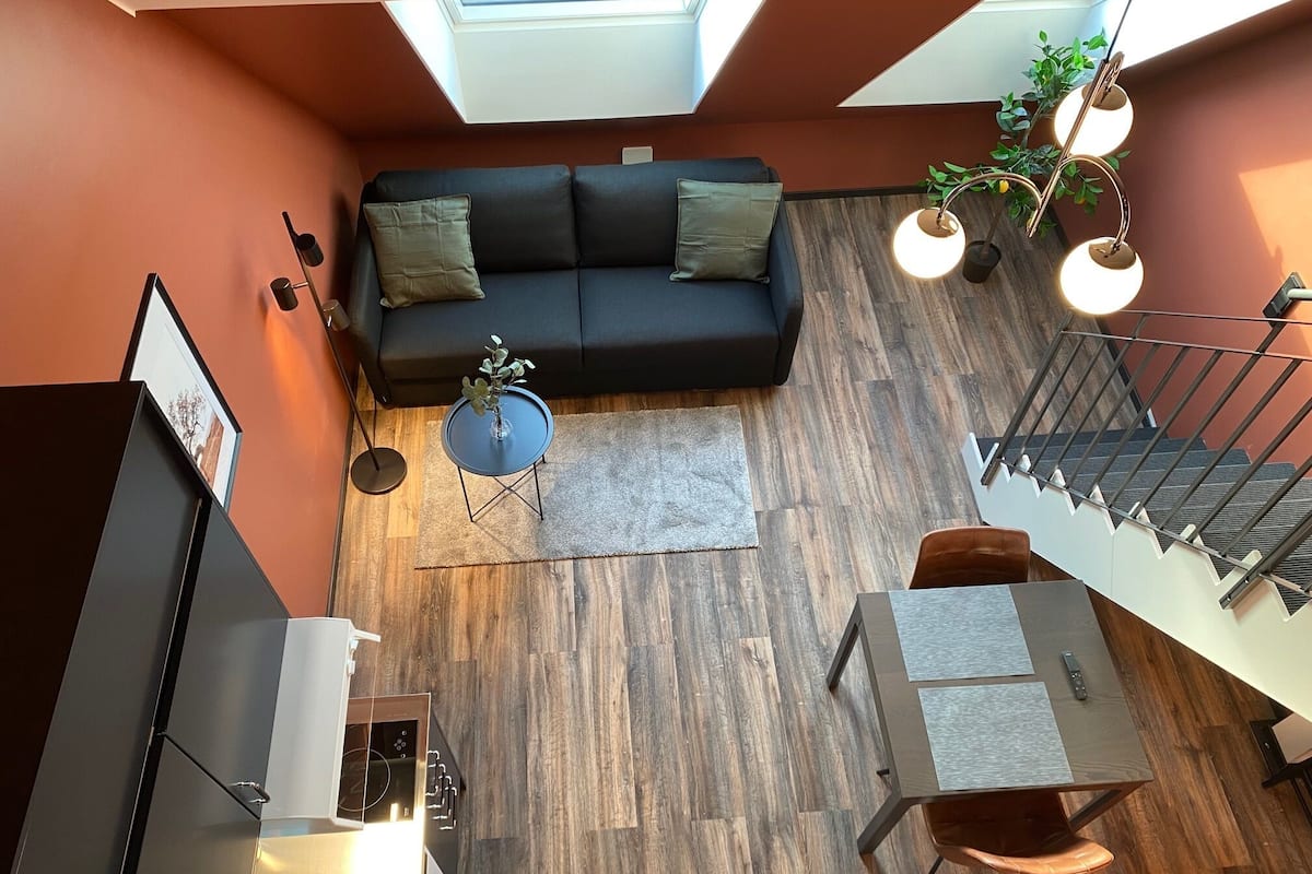 A modern interior with a black sofa, a small round table, a dining area, and a staircase.