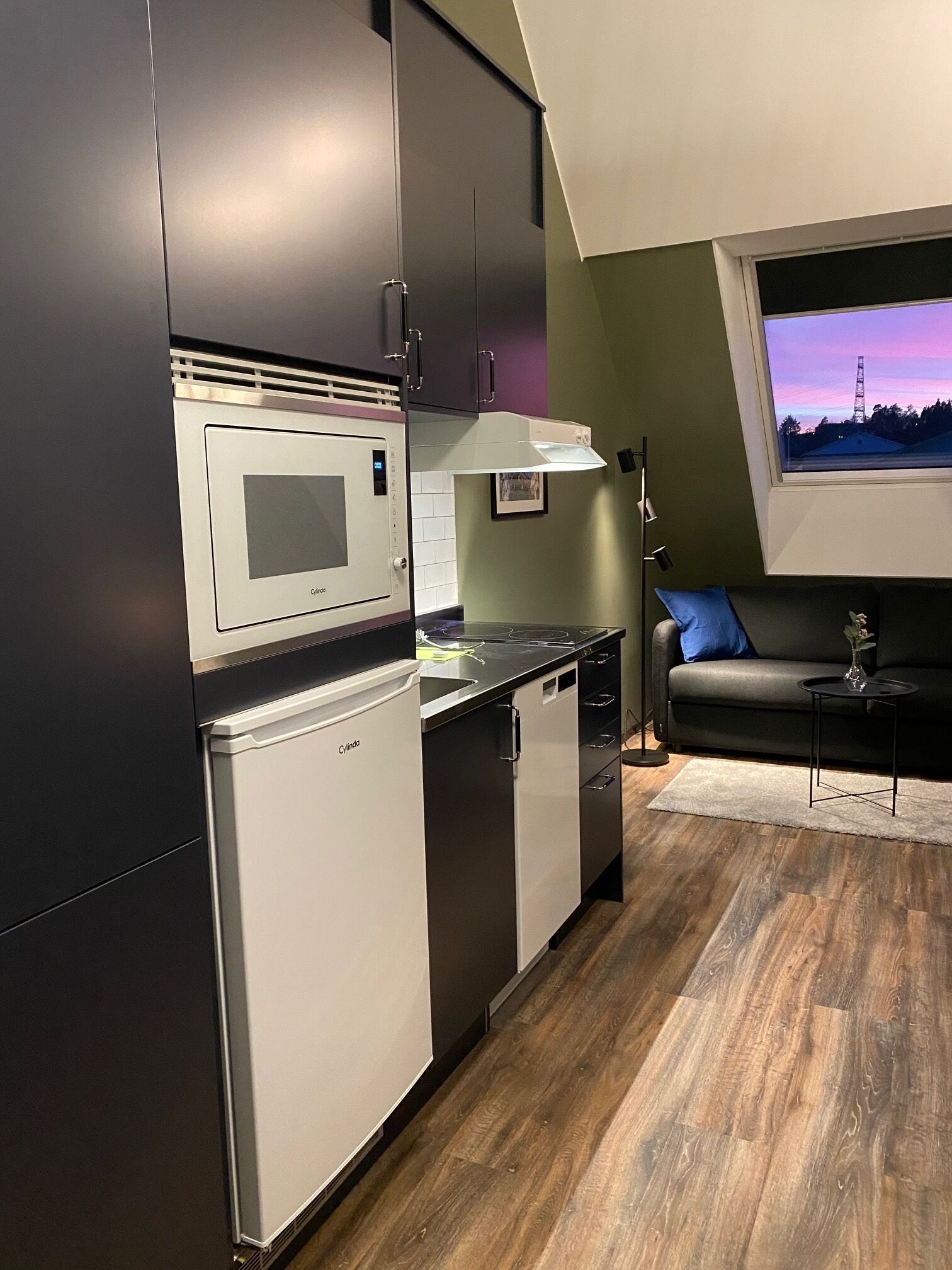A compact kitchen with modern appliances, a dining area with a sofa, and a window with a view of a tower.