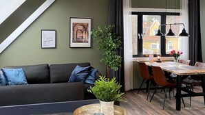 A modern loft apartment with a dining area, a living room with a sofa, and a kitchen counter with a plant and glasses.