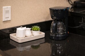 A kitchen counter with a coffee maker, a small potted plant, and a tray with two white containers.