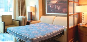 A hotel room with a bed, a chair, a table, and a lamp.