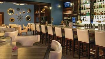 A bar area with multiple seating options, including bar stools and tables, and a variety of bottles and glasses on shelves.