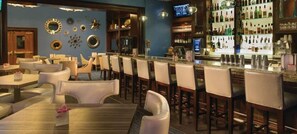 A bar area with multiple seating options, including bar stools and tables, and a variety of bottles and glasses on shelves.