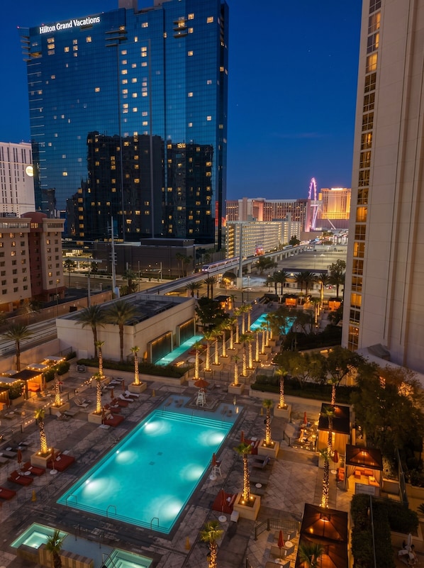 A hotel with a swimming pool, outdoor seating, and a view of the city skyline.