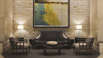 A lobby with a stone wall, a large abstract painting, a leather sofa, two armchairs, a coffee table, and two lamps.