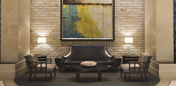A lobby with a stone wall, a large abstract painting, a leather sofa, two armchairs, a coffee table, and two lamps.