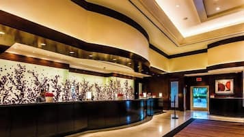 A modern hotel lobby with a curved reception desk, a large abstract wall art piece, and a digital display screen.