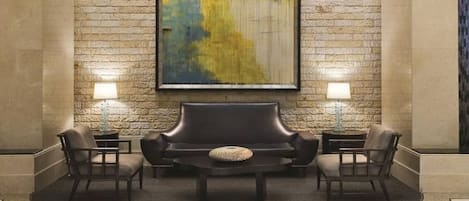 Un vestíbulo con pared de piedra, un cuadro abstracto de gran tamaño, un sofá de cuero, dos mesitas de noche con lámparas y cuatro sillas.