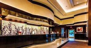 Una hall moderna di un hotel con una reception dalla forma curva, un’ampia opera d’arte astratta a parete e uno schermo digitale.