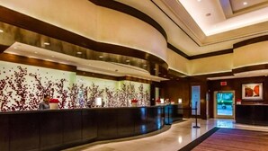 A modern hotel lobby with a curved reception desk, a large abstract wall art, and a television screen displaying a scenic view. - Luxury Studio | MGM Signature | Sleeps 4 | Strip View | No Resort Fee (LAS VEGAS)