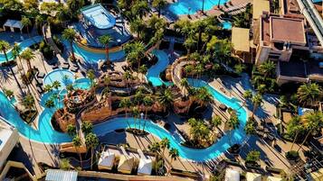 An aerial view of a resort with multiple swimming pools, palm trees, and a winding pathway.
