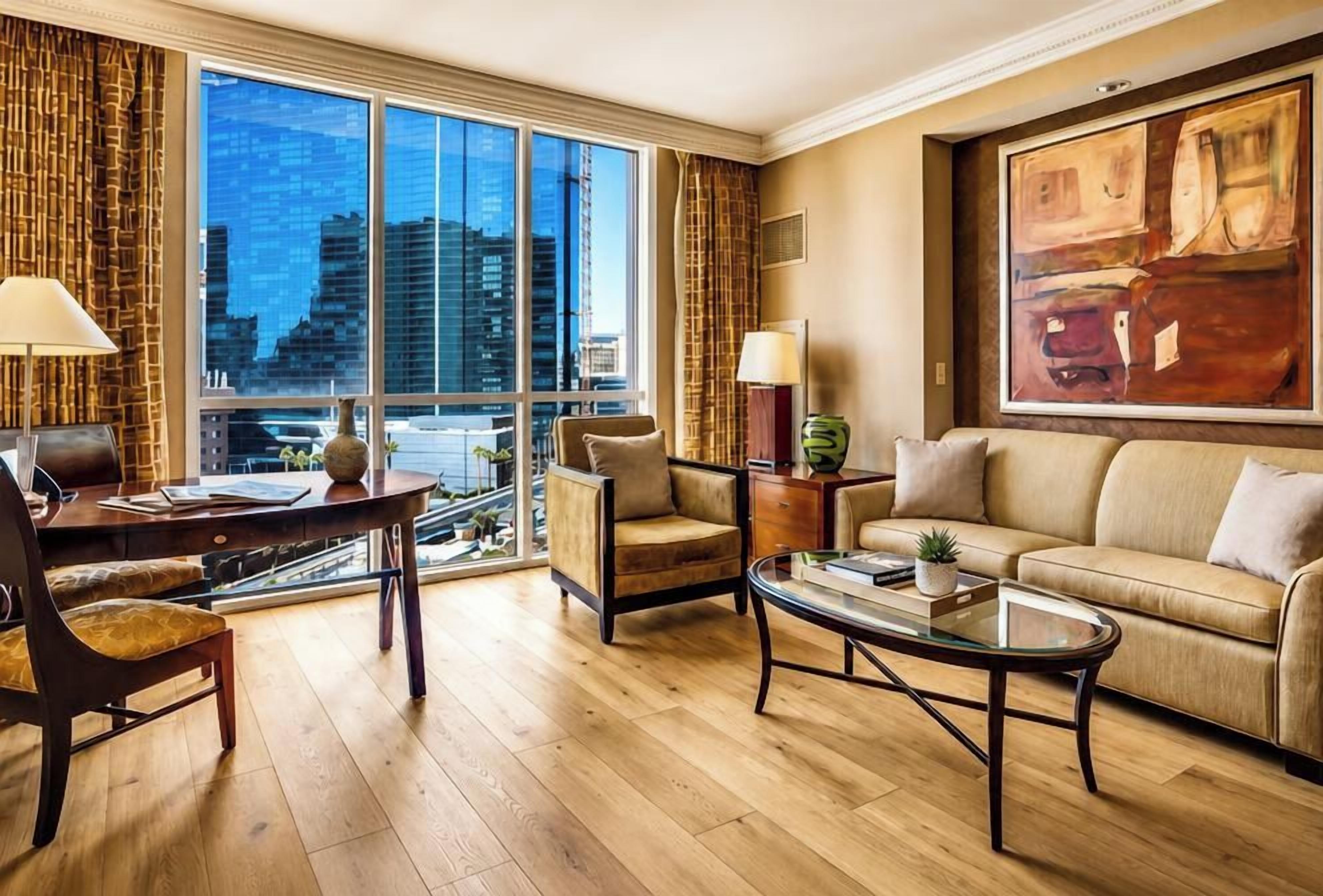 A modern hotel room with a large window, a sofa, a coffee table, and a chair.