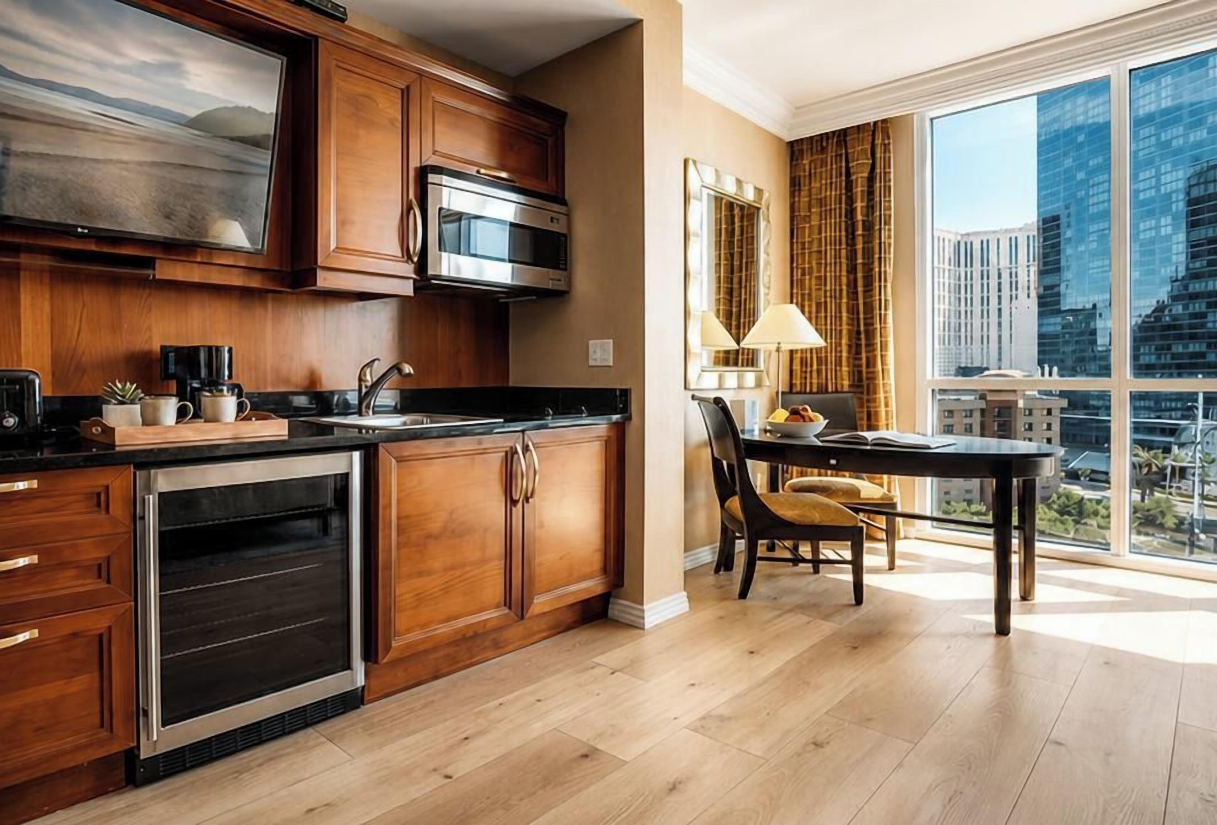 A modern kitchen with wooden cabinets, stainless steel appliances, and a dining area with a view of the city.