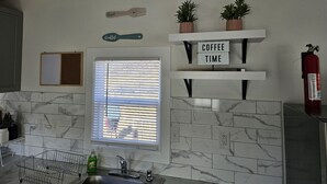 A kitchen with marble tiles, a window with blinds, a sink, a dish rack, and a 'Coffee Time' sign on a shelf. - Emmar Blue + Fishing Lake/ Pond  (Charlotte)