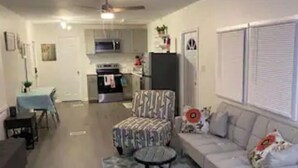 A living room with a sofa, a patterned armchair, a small round table, and a dining area with a table and chairs. - Emmar Blue + Fishing Lake/ Pond  (Charlotte)