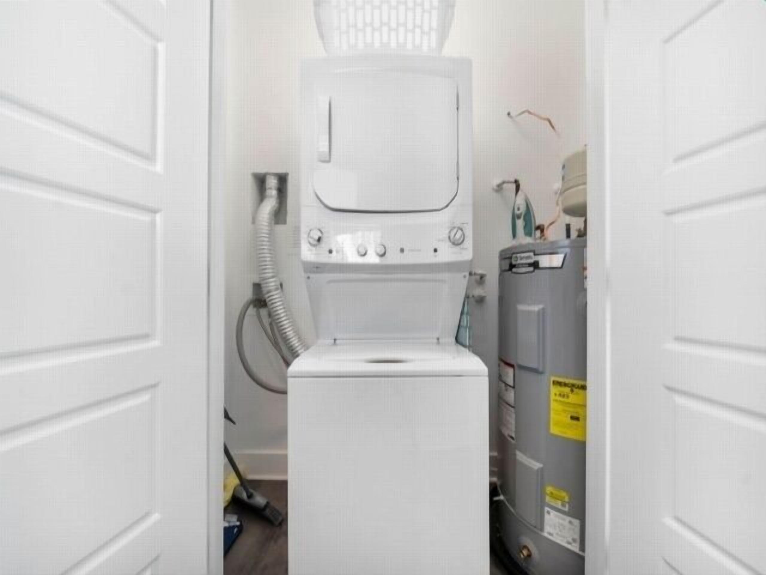 A compact laundry room with a front-loading washer and dryer, a water heater, and a visible electrical outlet.