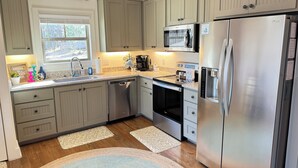 A kitchen with light wood cabinets, stainless steel appliances, a built-in microwave, and a refrigerator. - Cozy 2-bedroom cabin near Lake Martin (Eclectic)