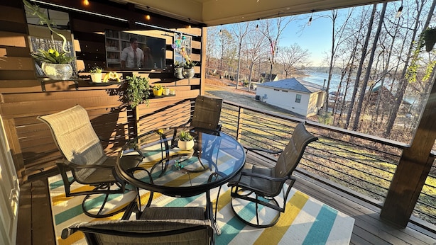 A cozy outdoor seating area with a glass table and chairs, surrounded by wooden railings and potted plants. - Cozy 2-bedroom cabin near Lake Martin (Eclectic)