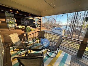 Un rincón exterior acogedor con una mesa y sillas de vidrio, rodeado de barandas de madera y macetas con plantas.