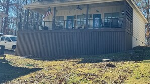 A small, single-story building with a sloped roof, a balcony with a railing, and an American flag. - Cozy 2-bedroom cabin near Lake Martin (Eclectic)