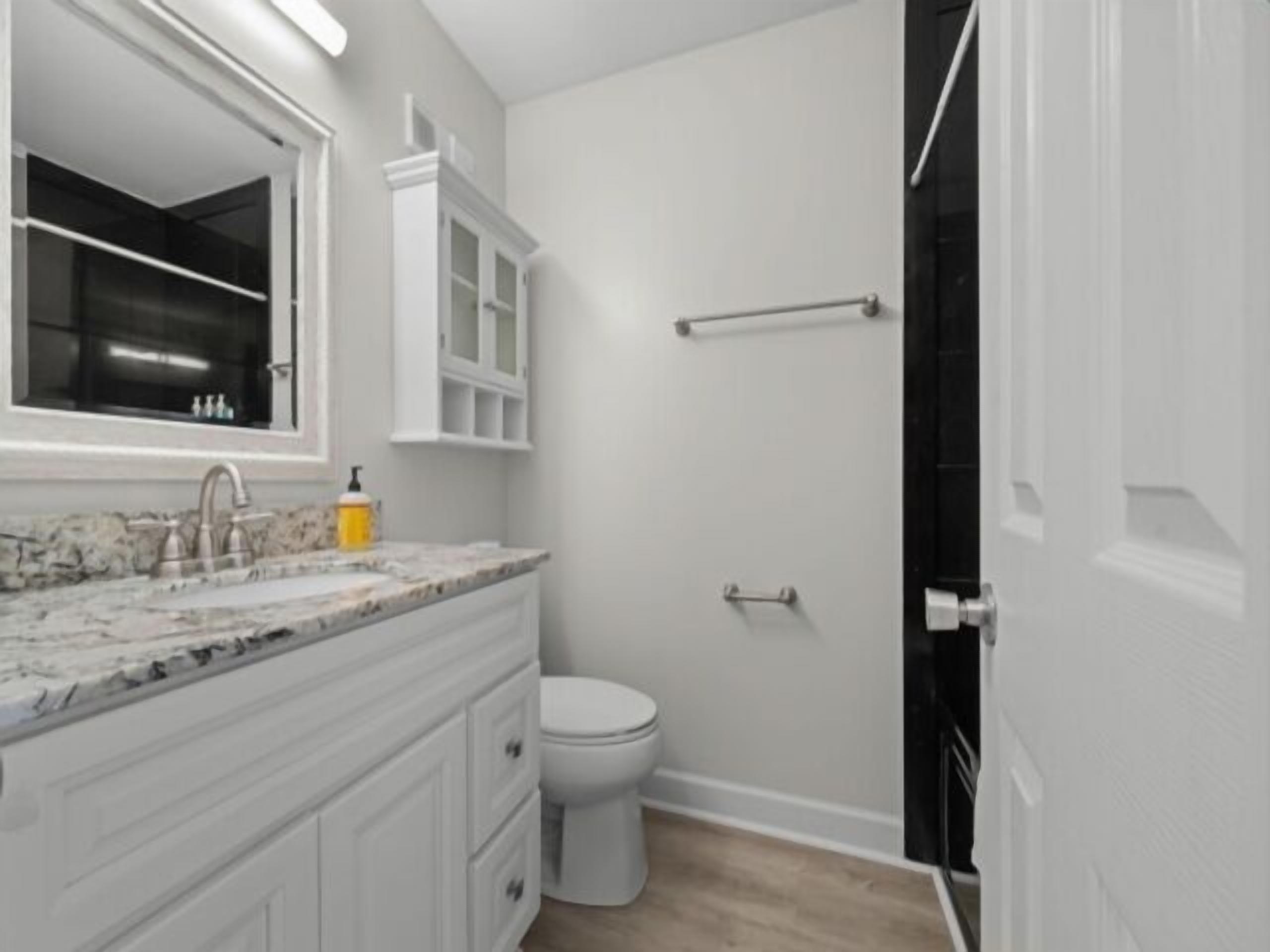 A bathroom with a marble sink, white cabinets, a toilet, and a black door.