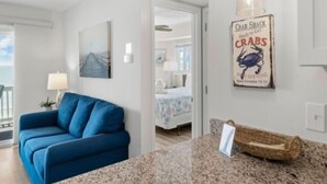 A room with a blue sofa, a granite countertop, a hanging light fixture, and a wall sign advertising a crab shack. - A Beach Dream 1 Bedroom Condo by RedAwning (Carolina Beach)