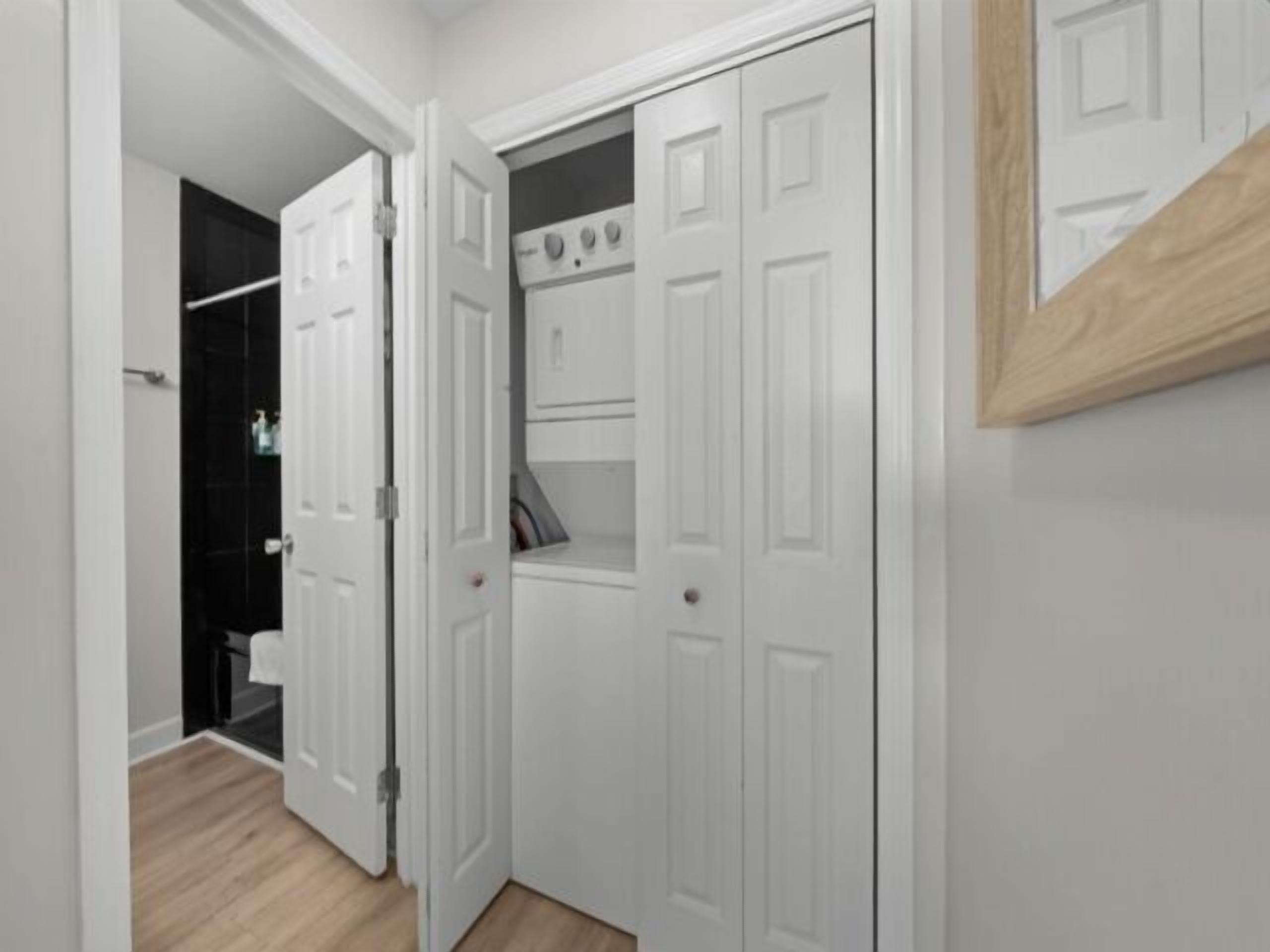 Ein Flur mit weißen Türen, Holzboden und einem schwarzen Kleiderschrank im Hintergrund.