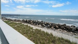 A coastal view with a rocky breakwater, ocean waves, and a distant pier. - A Beach Dream 1 Bedroom Condo by RedAwning (Carolina Beach)