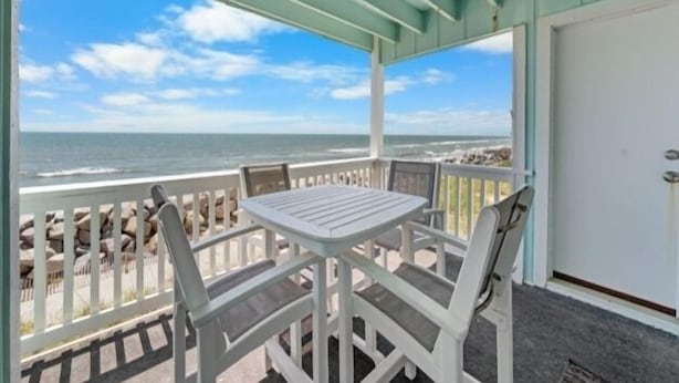 A covered outdoor seating area with a table and chairs, overlooking the ocean. - A Beach Dream 1 Bedroom Condo by RedAwning (Carolina Beach)