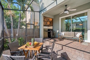 Une terrasse extérieure avec une table en bois, des chaises en osier, un canapé et un barbecue.