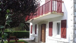A two-story building with a balcony, a stone facade, and two picnic tables in the yard. - GITE RURAL 4 PERS. NEAR ST JEAN PIED DE PORT (Ahaxe-Alciette-Bascassan)