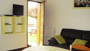 A room with a black sofa, a small table, a yellow shelf unit, and a door leading to an outdoor area with a picnic table. - GITE RURAL 4 PERS. NEAR ST JEAN PIED DE PORT (Ahaxe-Alciette-Bascassan)