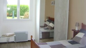 A bedroom with a bed, a chair, a bedside table, and a window with a view of greenery. - GITE RURAL 4 PERS. NEAR ST JEAN PIED DE PORT (Ahaxe-Alciette-Bascassan)