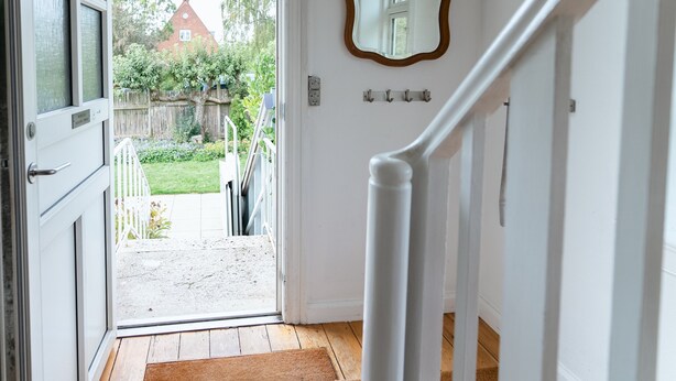 A hallway with a wooden staircase, a white door leading outside, and a mirror on the wall.