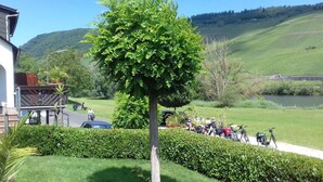 A tree-lined pathway with bicycles parked along the side, a clear view of a lake, and a hilly landscape in the background. - Moselstrand 2 uniquely beautiful location directly on the Moselle, on the Moselle cycle path g (Lösnich)